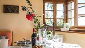Une table à manger dressée avec des assiettes, des verres et une bouteille de vin, avec une fenêtre et des plantes en arrière-plan.