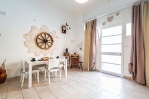 Quarto com uma mesa branca, cadeiras, um objeto decorativo na parede, um relógio e uma porta de correr com cortinas.
