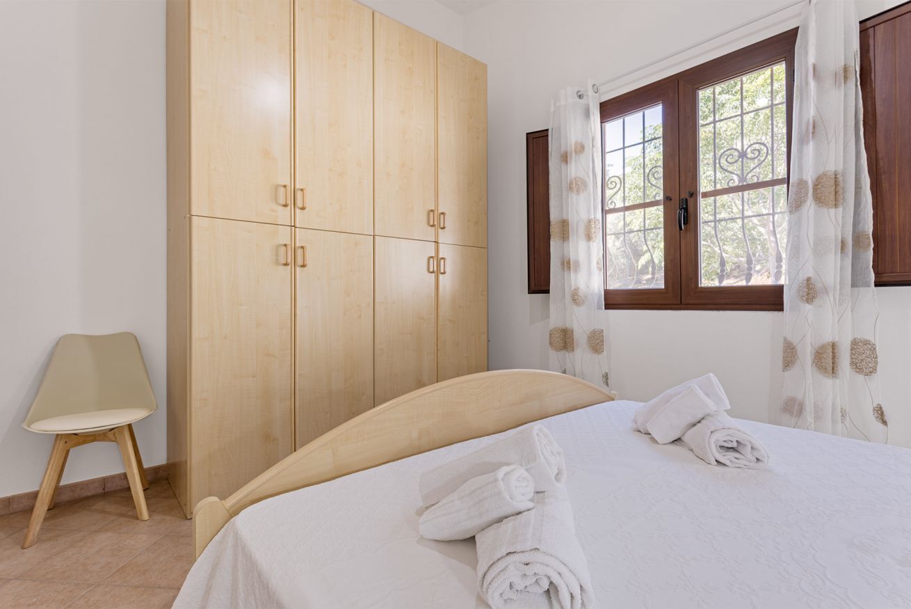 Een slaapkamer met een bed, een houten kledingkast, een stoel en een raam met gordijnen.