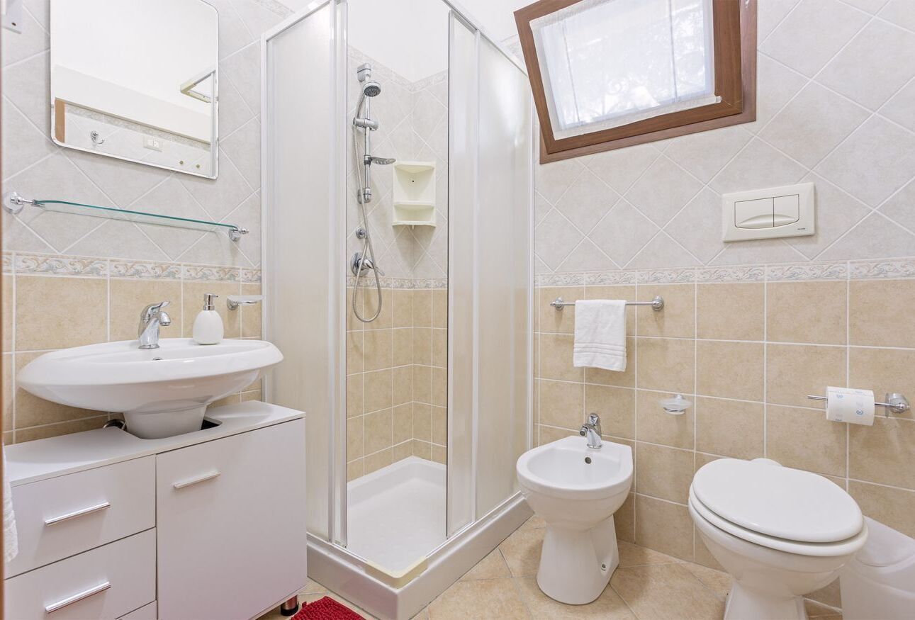 A bathroom with a shower, sink, bidet, and toilet.