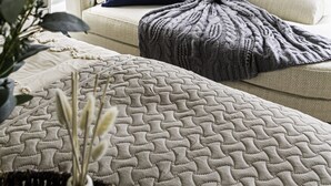Une pièce chaleureuse avec un canapé beige, un coussin bleu et un plaid à motifs.