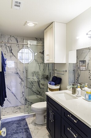 Un bagno con doccia vetrata, un WC bianco, mobili scuri e uno schienale in marmo.