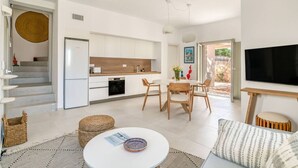 A modern kitchen with white cabinets, a built-in oven, and a dining area with a round table and chairs. - Villa Alma - Aliki Center (Aliki)