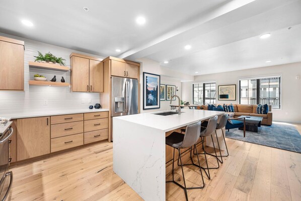 A modern kitchen with wooden cabinets, a marble island, and a dining area with a sofa and chairs.