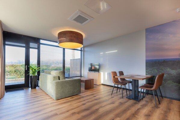 A modern living room with a sofa, dining table, chairs, a TV, and a large window with blinds.