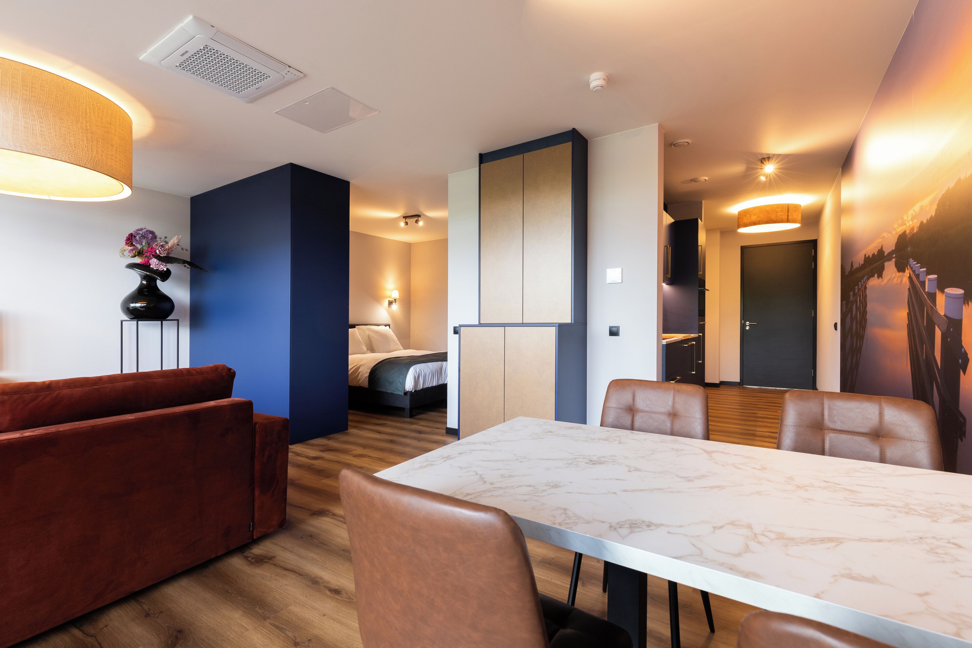 Una habitación de hotel moderna con zona de comedor, cama, baño y un ventanal grande.