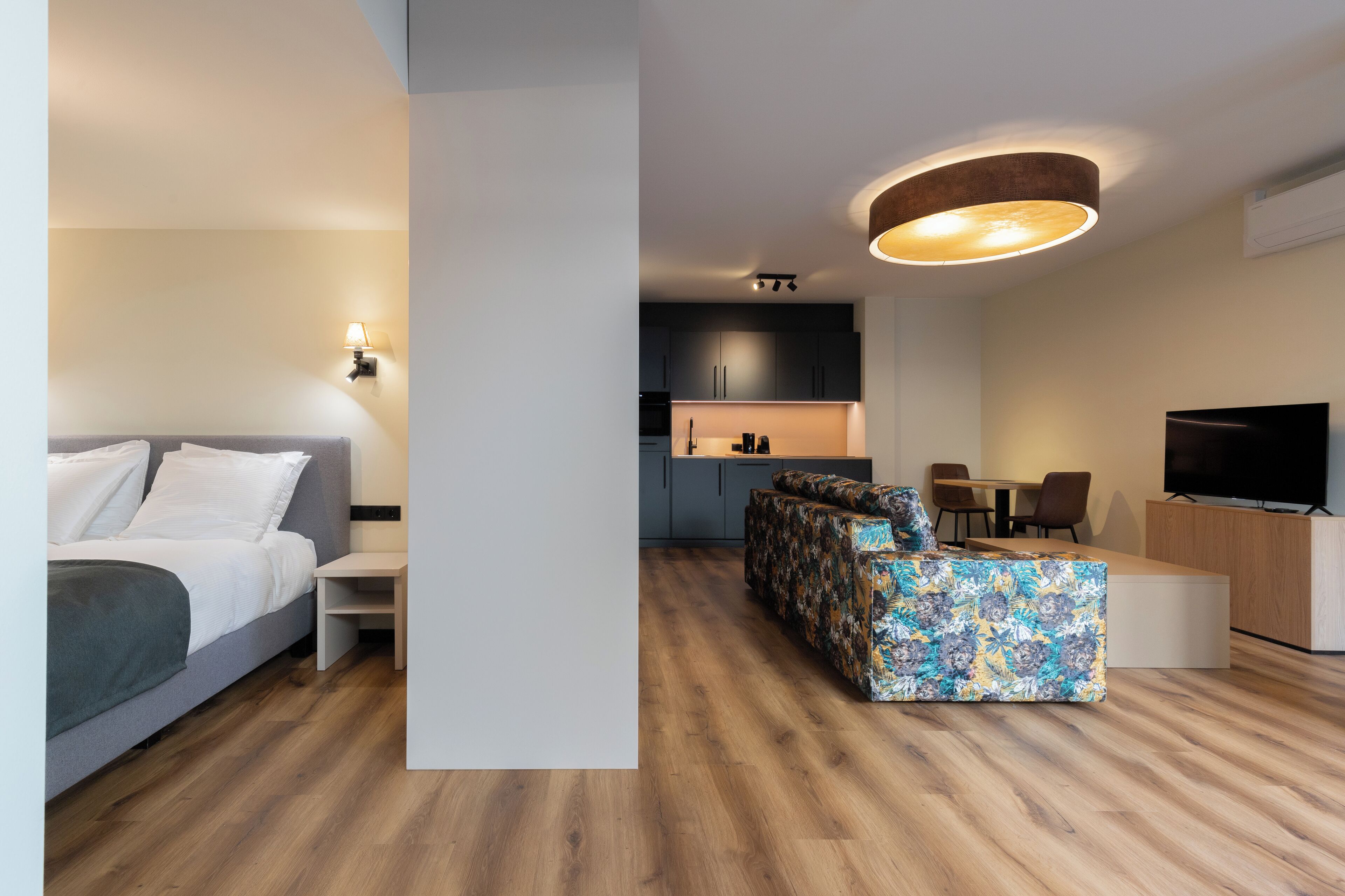 Un espacio de estar moderno con una cama, un sofá, un televisor y una cocina.