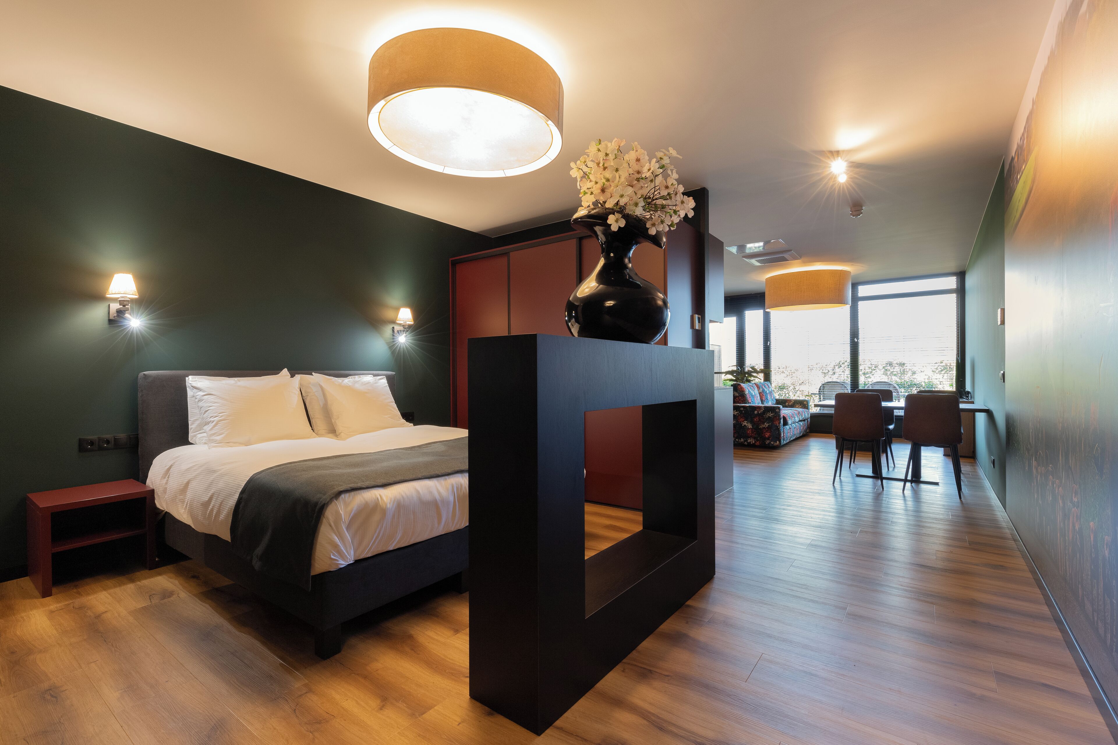 Une chambre moderne comprenant un lit, des tables de chevet, une grande fenêtre et un coin repas avec des chaises et une table.