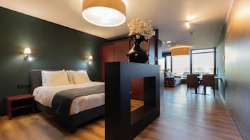 Une chambre moderne comprenant un lit, des tables de chevet, une grande fenêtre et un coin repas avec des chaises et une table.