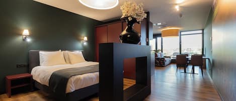A modern bedroom with a bed, bedside tables, a large window, and a dining area with chairs and a table.