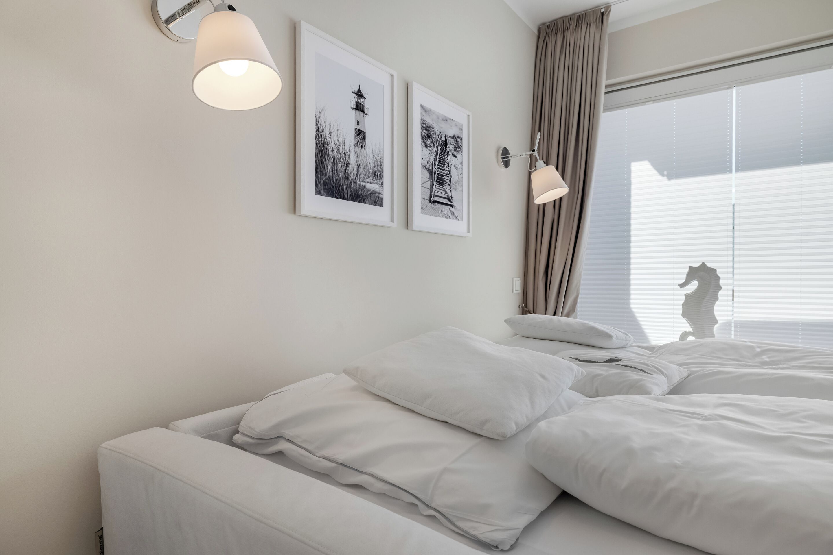 A bedroom with a bed, two wall-mounted lamps, and two framed pictures.