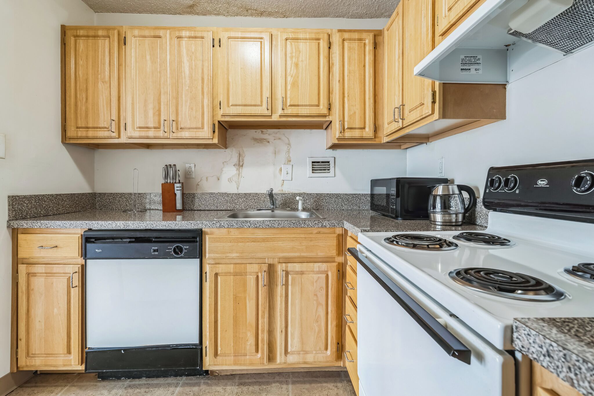 Una cocina con armarios de madera, lavavajillas, estufa y microondas.