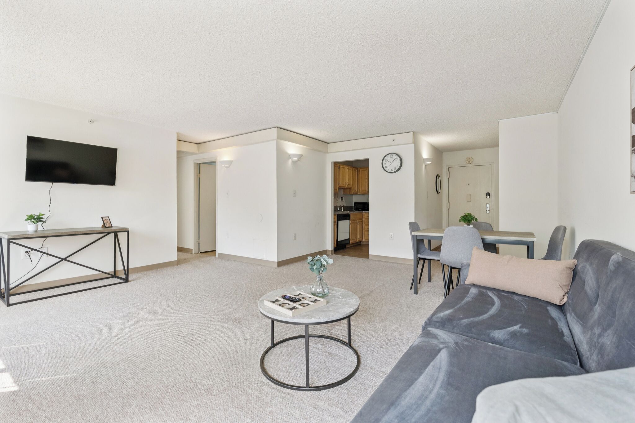 Ein modernes Wohnzimmer mit grauem Sofa, rundem Couchtisch, Flachbildfernseher und Essbereich mit Tisch und Stühlen.