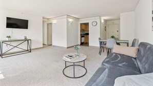 A modern living room with a grey sofa, a round coffee table, a flat-screen TV, and a dining area with a table and chairs. - Legacy at Imperial Village 417 I 2 Bed 2 Bath (Ric hmond)