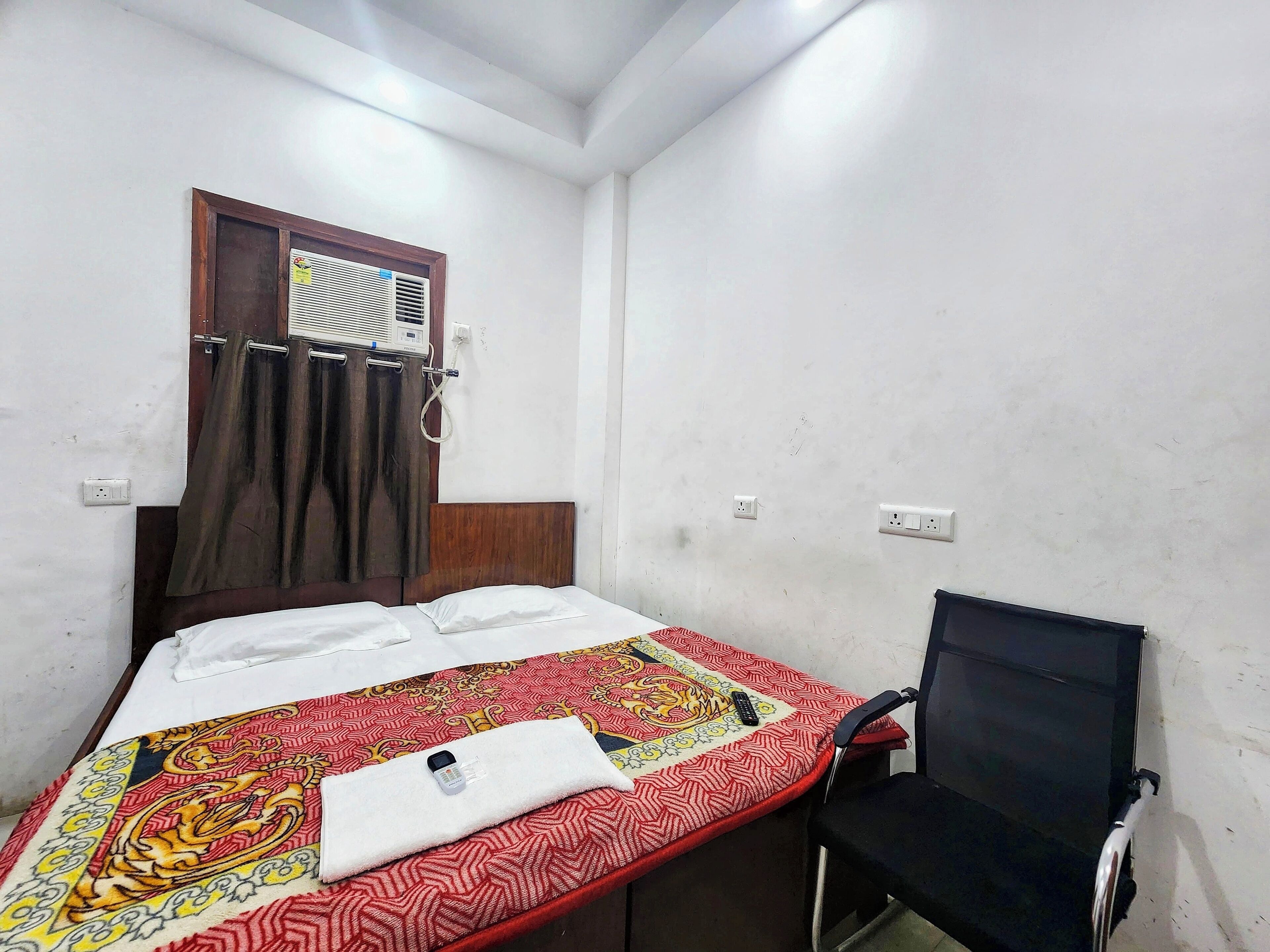A small, simple room with a bed, a chair, and a window with curtains.
