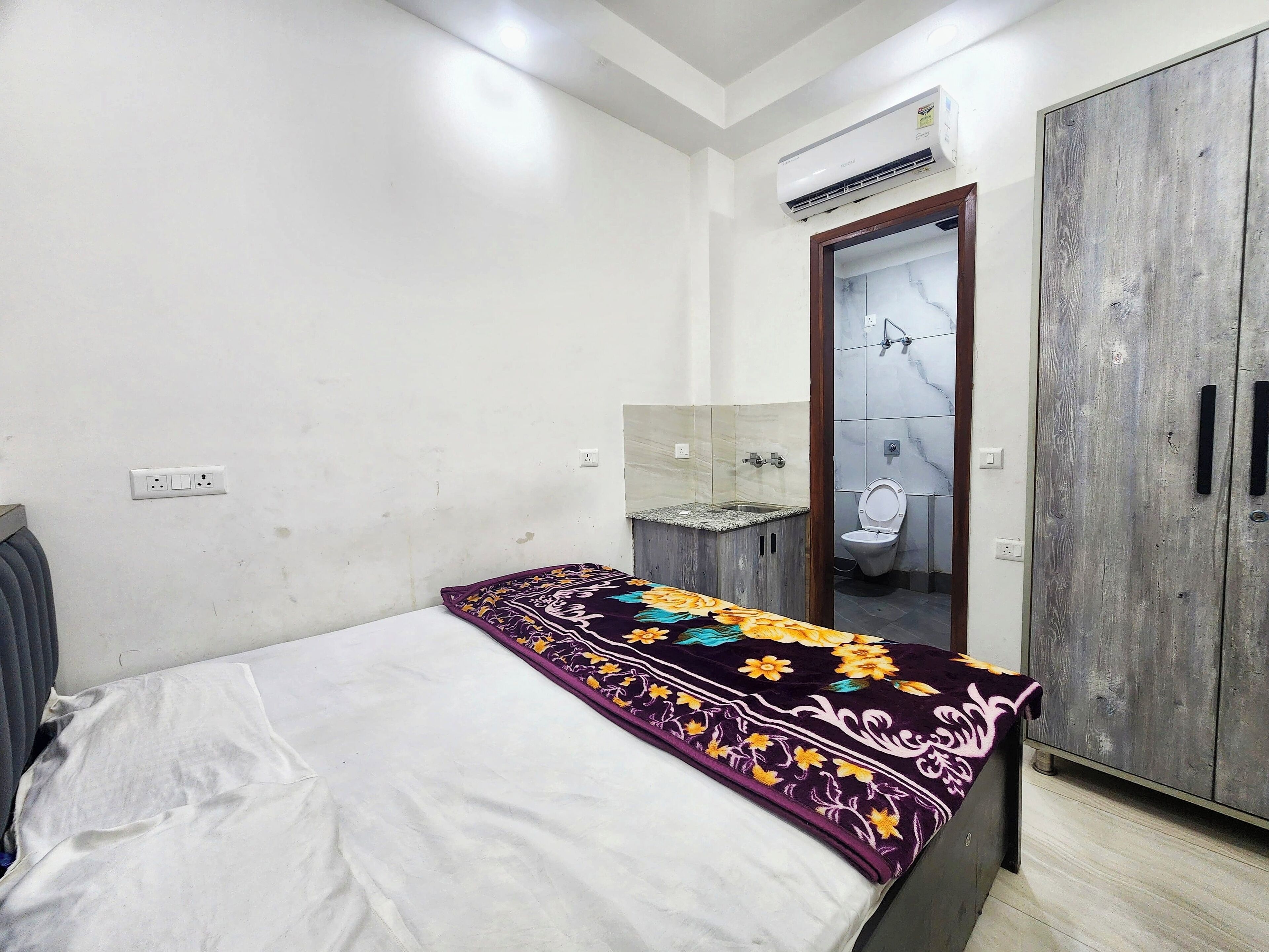 Une chambre comprenant un lit, une armoire, une salle de bain avec des toilettes et un lavabo, ainsi qu’un appareil de climatisation.