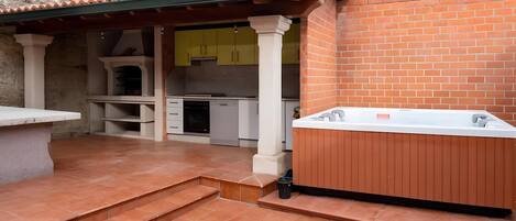 A patio area with a hot tub, a stone bench, and a kitchen with yellow cabinets.