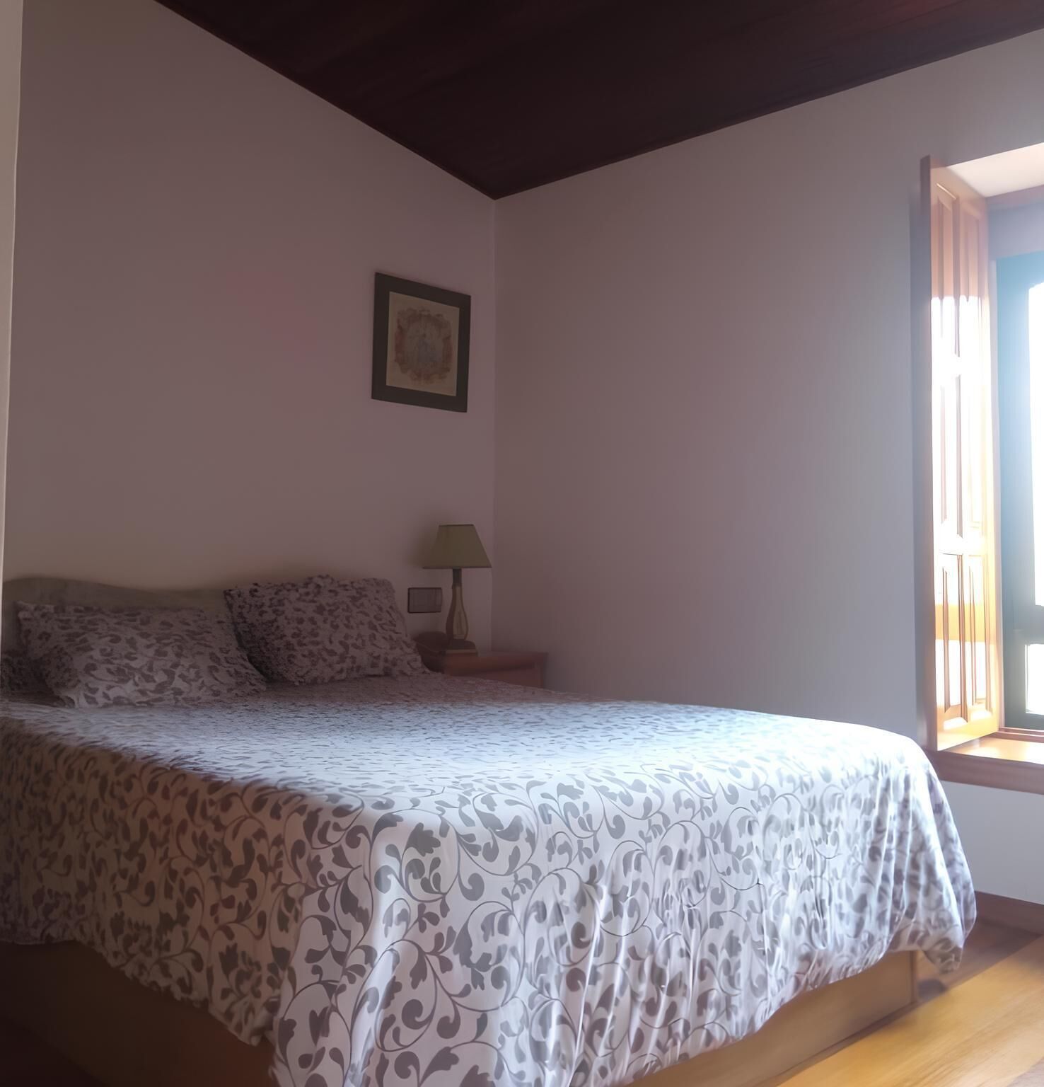 A bedroom with a bed, a nightstand, a lamp, and a framed picture on the wall.