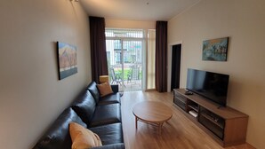 A modern living room with a leather sofa, a round coffee table, a flat-screen TV, and a sliding glass door leading to an outdoor area. - New apartment 5min to airport at Kokstad train station (Vestland)