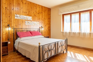 Un dormitorio con pared de paneles de madera, una cama con estructura de metal, una mesita de noche y una ventana con cortinas.