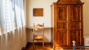 A room with a wooden desk, a chair, a wardrobe, and a window with curtains.