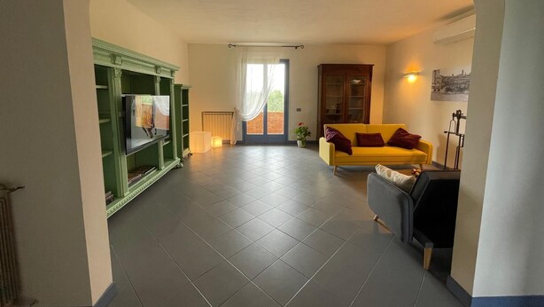 A spacious living area with a green entertainment unit, a yellow sofa, and a black armchair.