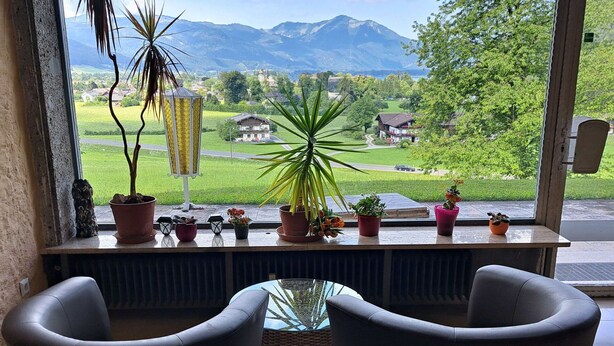 A room with two chairs facing a window overlooking a green landscape with houses and mountains. - Lovely apartment for 4 guests with WIFI, TV and patio (Strobl)