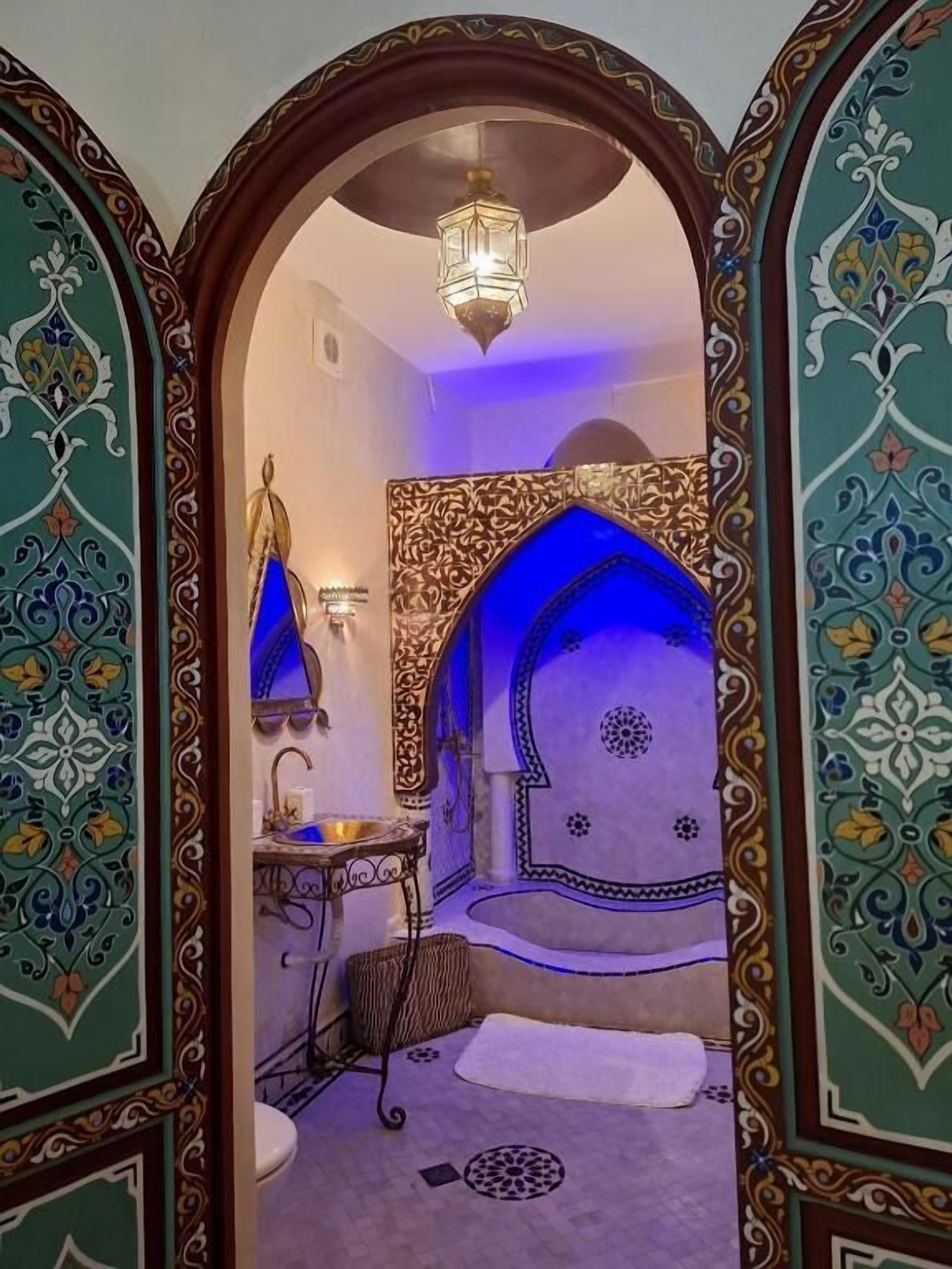 A traditional bathroom with ornate tile work, a hanging light fixture, and a blue accent wall.