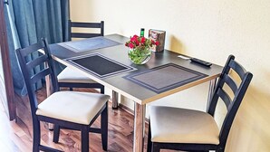 A dining table with four chairs, a vase of red flowers, a remote control, and a book on the table.
