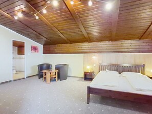Een kamer met houten plafond, een bed, een bureau, een stoel en een klein tafeltje.