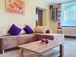 Een woonkamer met een bank, twee paarse kussens, een houten salontafel en een schilderij aan de muur.
