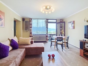 A living room with a sofa, a coffee table, a dining area with chairs, a TV, and a view of the outdoors. - Cosy apartment for 4 people with WIFI, TV and balcony (Strobl)
