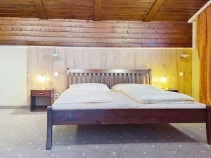 A wooden-framed bed with two nightstands, each with a lamp, in a room with wooden walls and a sloped ceiling. - Cosy apartment for 4 people with WIFI, TV and balcony (Strobl)