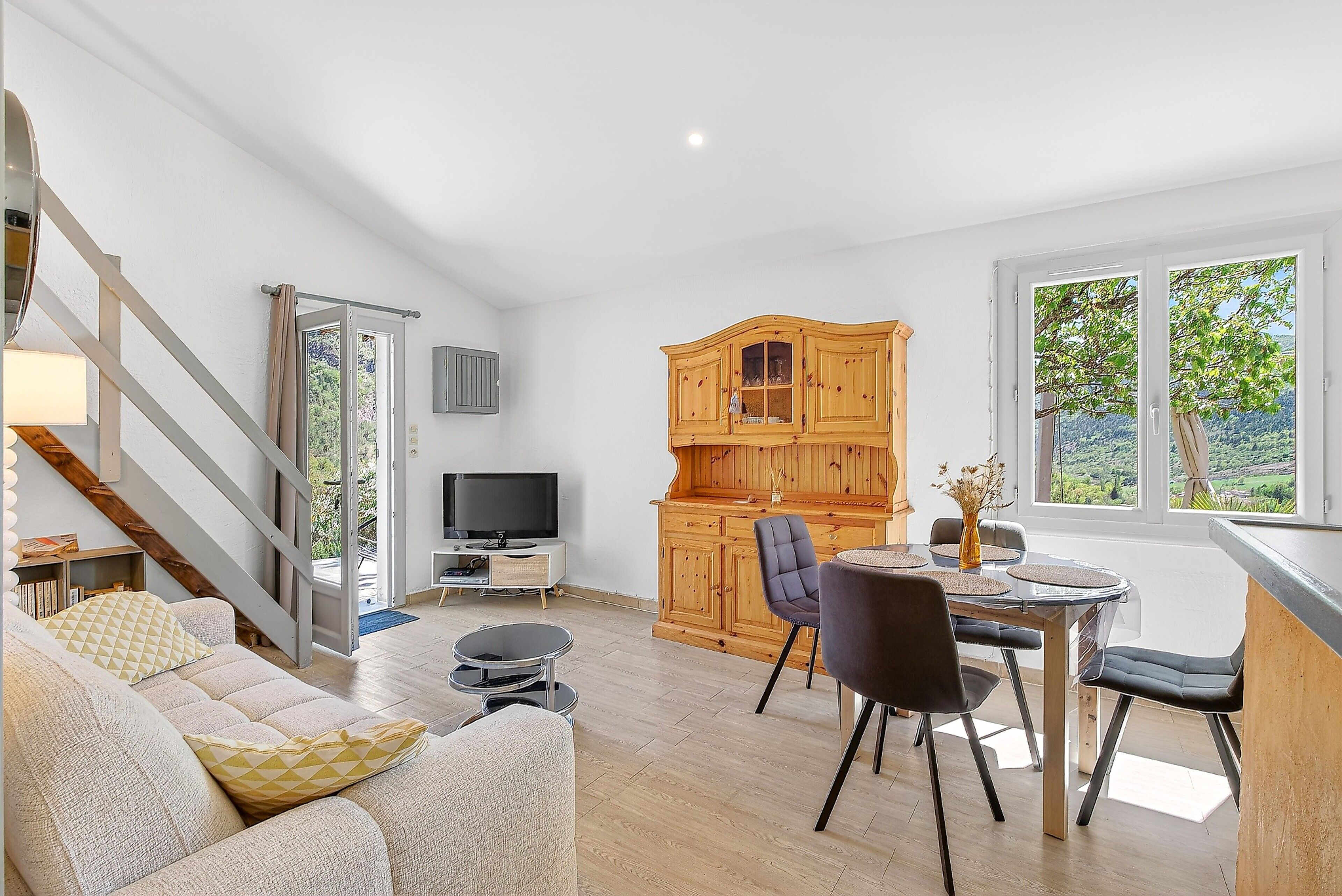 Un espacio habitable moderno con sofá, mesa de comedor, sillas, televisor, armarios de madera y una escalera.