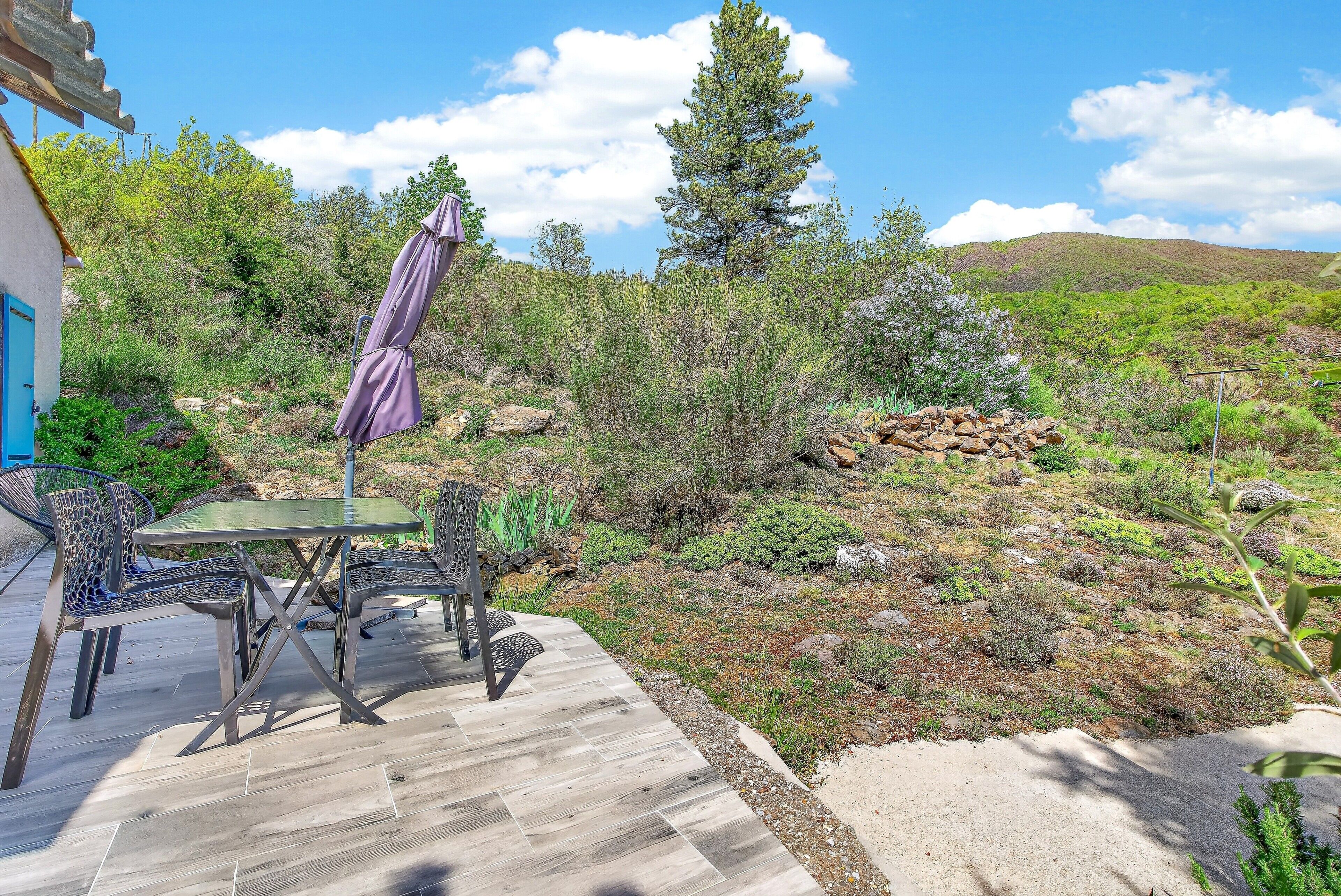 An outdoor patio with a table and chairs, surrounded by natural vegetation and a view of a hill.