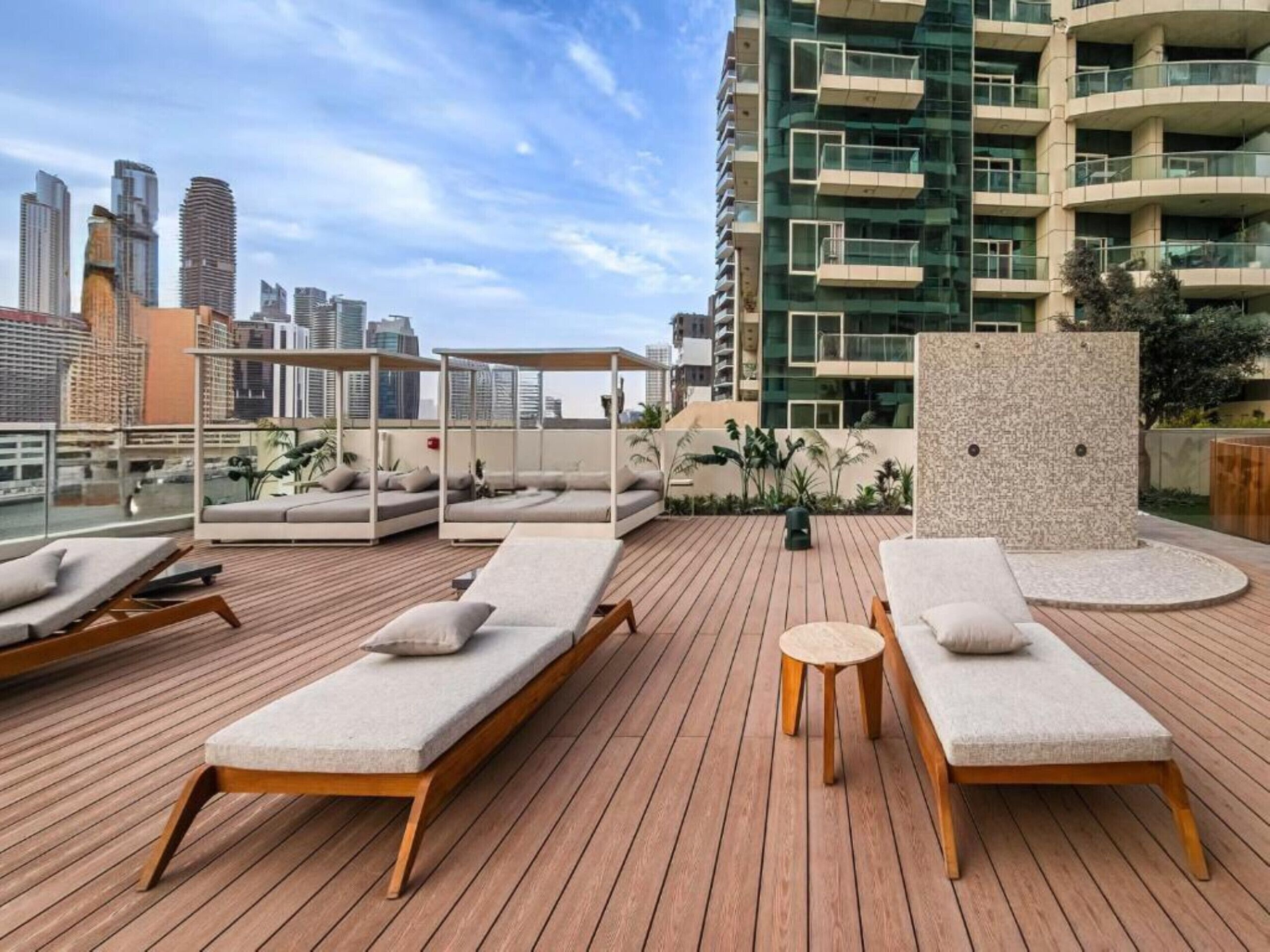 Un salon sur le toit, doté de chaises longues et d’une petite table, offrant une vue panoramique sur la ville et ses bâtiments modernes.