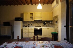 Une cuisine compacte avec des meubles de rangement en bois, un four encastré et une table à manger avec des chaises.