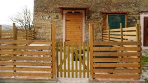 Un bâtiment rustique en pierre, doté d’un portail en bois, d’une porte et d’une fenêtre avec des volets.