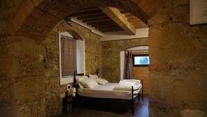 Une pièce rustique aux murs en briques apparentes, avec un plafond en bois, un lit à ossature métallique et une fenêtre agrémentée de rideaux.