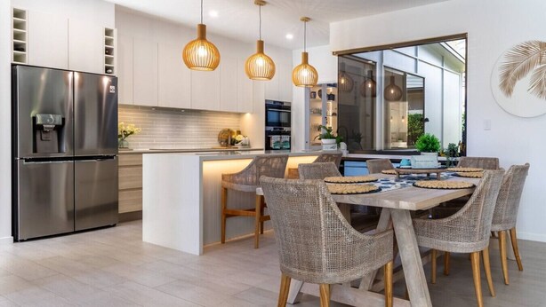 Een moderne keuken met een roestvrijstalen koelkast, een centraal keukenblok met een spoelbak en rieten stoelen rond een houten eettafel.