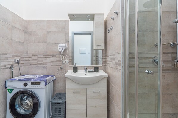 A modern bathroom with a washing machine, sink, mirror, and glass-enclosed shower.