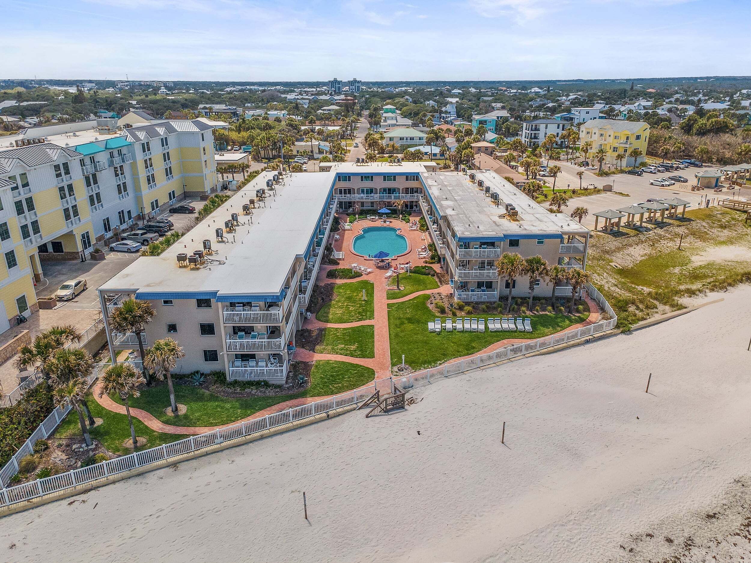A resort with a central pool, multiple buildings, and a beach area.