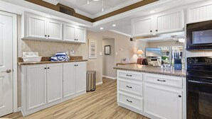 A kitchen with white cabinetry, a black oven, and a ceiling fan. - Beachfront Comfort w/ Pool, Patio & Steps to Flagler Avenue (New Smyrna Beach)