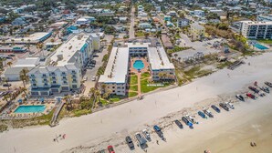 A coastal hotel with multiple buildings, a swimming pool, and a beach area with parked cars. - Beachfront Comfort w/ Pool, Patio & Steps to Flagler Avenue (New Smyrna Beach)