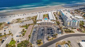 An aerial view of a coastal hotel with a parking lot, beach access, and ocean views. - Beachfront Comfort w/ Pool, Patio & Steps to Flagler Avenue (New Smyrna Beach)