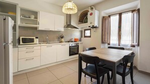 Une cuisine moderne avec des meubles blancs, un four à micro-ondes, un four traditionnel et une table à manger avec des chaises.