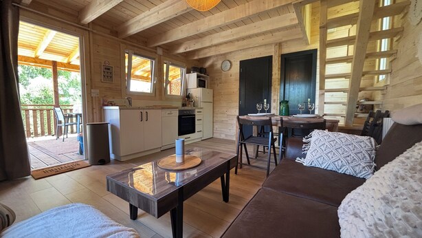 Ein gemütliches Holzhaus mit Küche, Essbereich und Wohnzimmer mit Sofa und Couchtisch.
