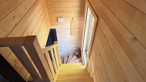Eine Holztreppe in einer Hütte, am Fuß befindet sich ein Hund.