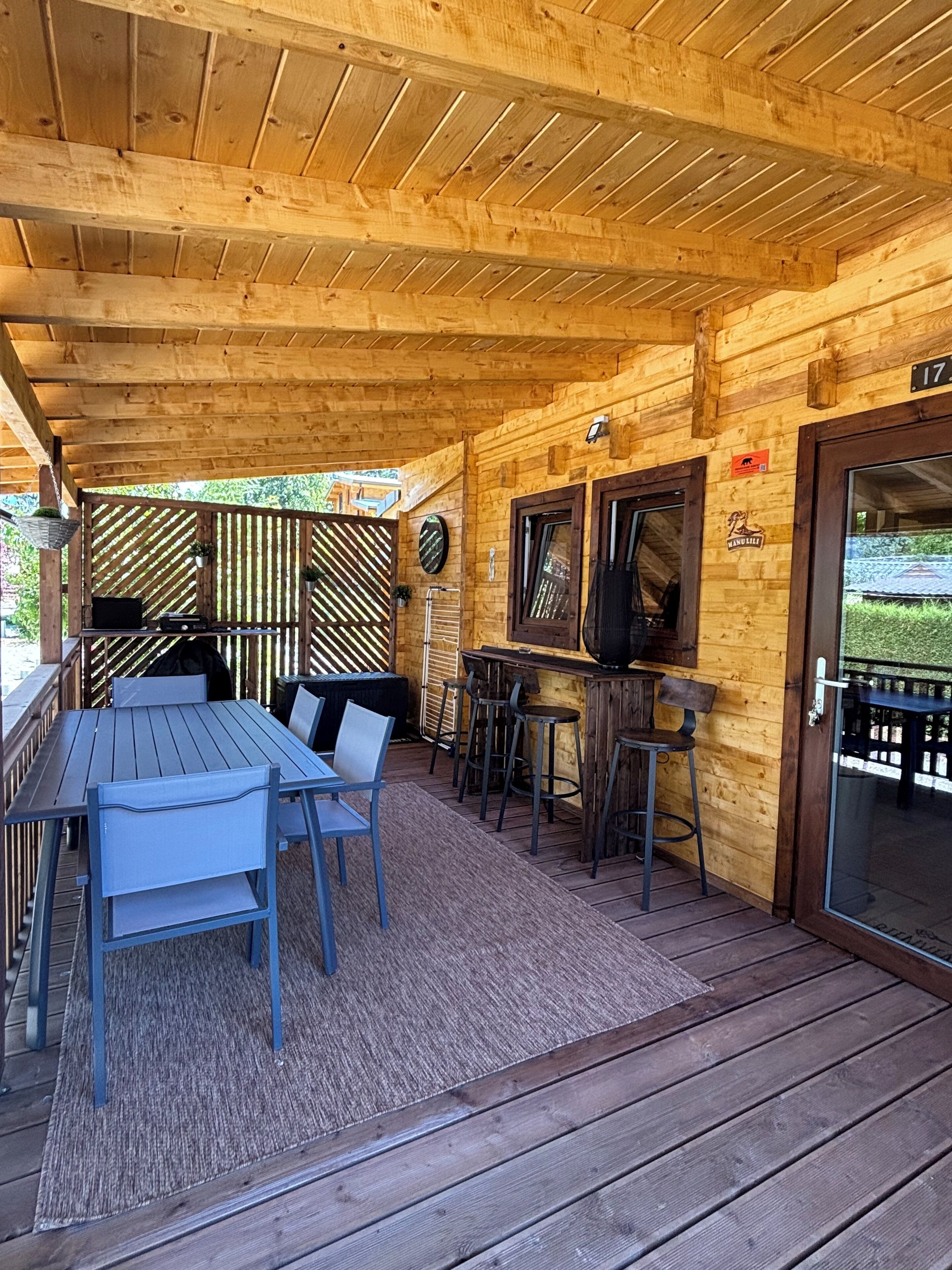 Une cabane en bois dotée d’un patio couvert comprenant une table et des chaises, un coin bar avec des tabourets et une porte portant le numéro 17.