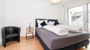 Ein modernes Schlafzimmer mit einem Bett, einem Sessel, einem Nachttisch und einem großen Fenster.